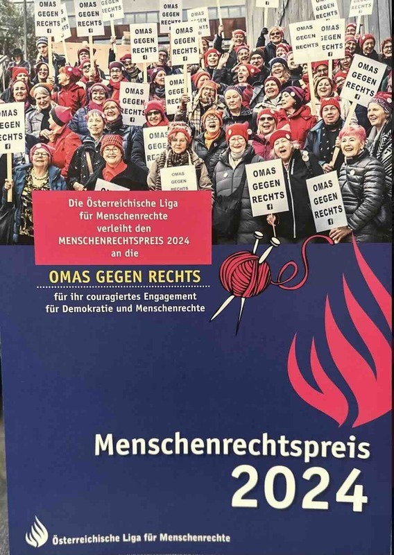 Photograph of group of Omas Gegen Rechts (English: Grandmas Against the Right) in their traidtional pink knit hats holding sign that reads "Menschenrechtspreis 2024" (English: Human Rights Prize 2024) given to them by LIGA